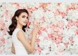 A woman stands gracefully in front of a vibrant flowerwall of flowers, exuding elegance and beauty.