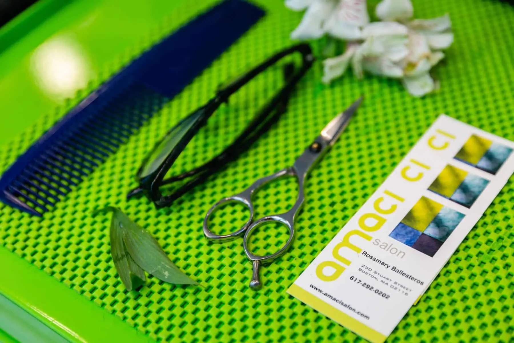 A green tray with scissors, comb, and amaci salon brochure neatly arranged on it.