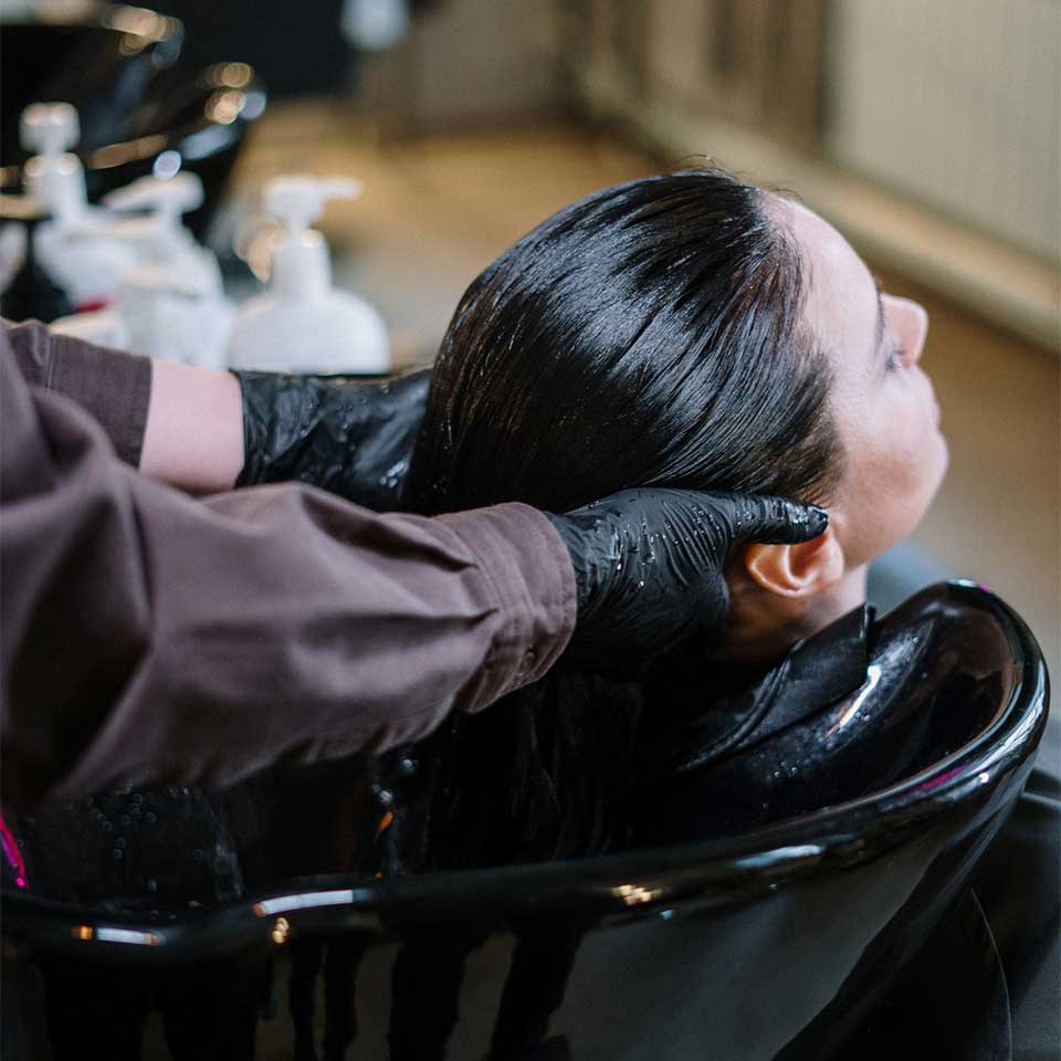 A woman enjoying a relaxing hair wash at a salon, with water flowing over her hair and a professional stylist attending to her.