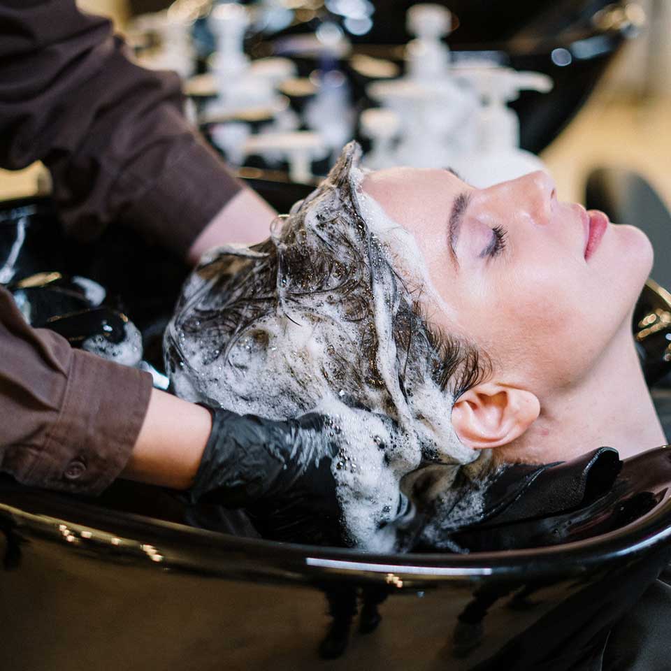 A woman enjoying a relaxing hair wash at a salon, with water flowing over her hair as she leans back comfortably.