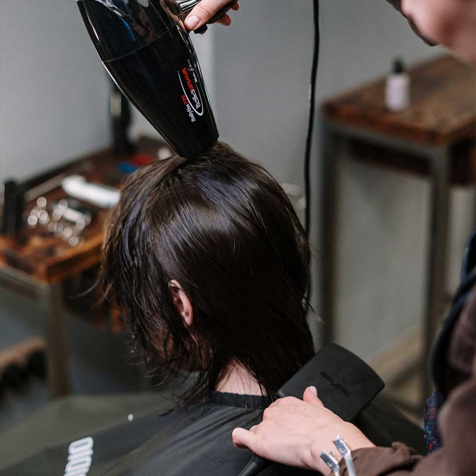 A woman at a hair salon getting her hair blow dried by a stylist.